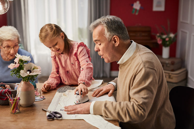 Family activity involving a child and adults at a table with paper and scissors.